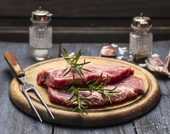raw meat with rosemary, garlic, salt and pepper on a wooden board with a fork