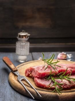 raw pork with rosemary on a wooden board with a fork, close up