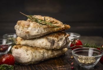 Stack of roast chicken breast with fried seasoning and tomatoes on dark wooden background
