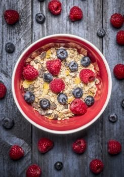 Oatmeal muesli with fresh berries in red bowl on blue rustic backgrund, top view. Sport, health and diet food concept.