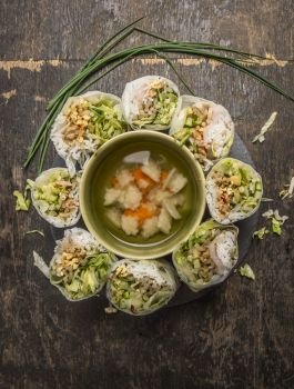 sliced rice rolls lined circle around a bowl of vegetable soup on wooden background top view