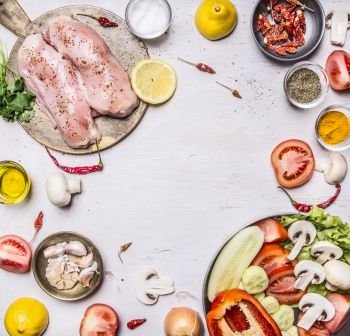 Several delicious raw turkey breast On a cutting board with seasoning a variety of fruits and vegetables laid out frame on rustic wooden background top view close up space for text