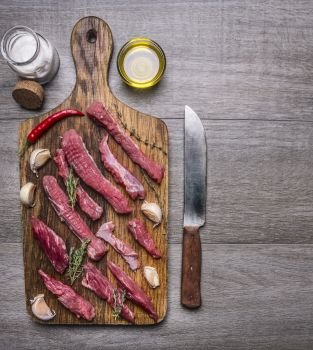 thinly sliced lamb with garlic on a cutting board with a knife for meat, butter and salt border ,with text area on wooden rustic background top view close up