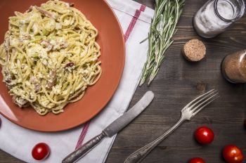 pasta with zucchini and turkey, ham and herbs on a brown plate on white napkin with vintage cutlery on wooden rustic background top view close up