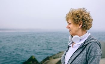 Senior sportswoman with headphones looking at the sea. Senior sportswoman looking at the sea