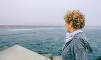 Unrecognizable senior sportswoman with headphones looking at the sea. Senior sportswoman looking at the sea