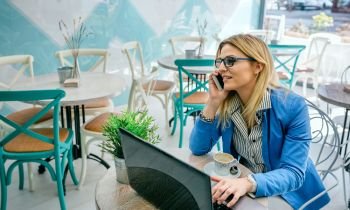 Businesswoman talking on phone and using laptop in a cafe. Woman talking on phone with laptop