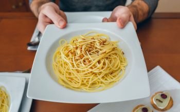 Detail of hands of unrecognizable man showing spaghetti with crispy worms dish. Hands of man showing spaghetti with worms dish