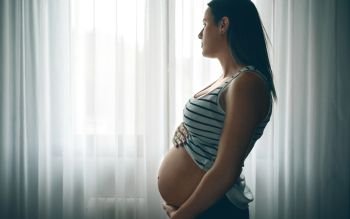 Pregnant caressing her nacked belly in front of a curtain. Pregnant caressing her nacked belly