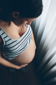 Top view of pregnant looking her belly in front of a curtain. Pregnant woman looking her belly