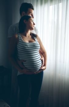 Pregnant woman caressing her belly embraced by her husband. Pregnant woman embraced by her husband