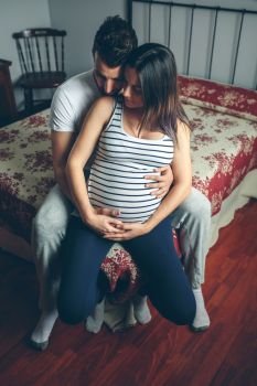Unrecognizable pregnant woman touching her belly embraced by her husband. Pregnant woman embraced by her husband