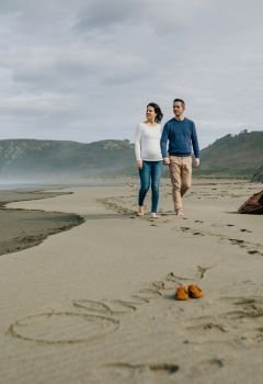 Parents taking a walk with baby name Oliver written in the sand next to his shoes. Selective focus on couple in background. Parents walking with baby name Oliver written in the sand