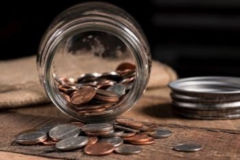Poverty concept image with a few small coins remaining in a glass savings jar on wooden table. Glass mason jar with a few coins inside to illustrate poverty