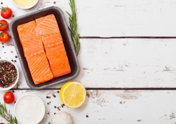 Plastic container with fresh salmon slice with oil tomatoes and lemon on wooden kitchen background