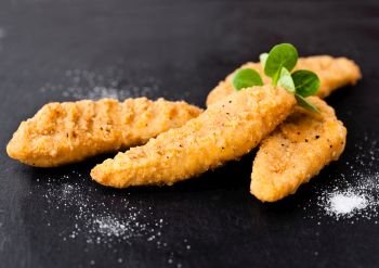 Fried chicken dippers on stone board with salt on black background
