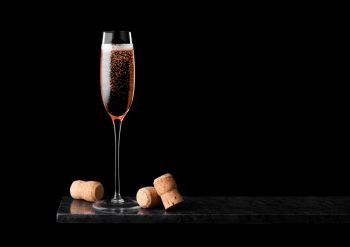 Elegant glass of pink rose champagne with cork on black marble board on black