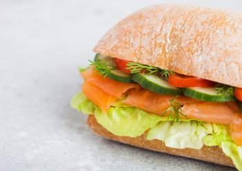 Fresh healthy salmon sandwich with lettuce and cucumber on white stone background. Breakfast snack