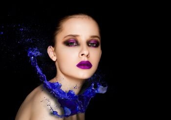 Blue paint splash over beauty makeup fashion model girl with purple smokey eyes abstract on black background