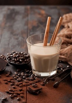Glass of Irish cream baileys liqueur with cinnamon coffee beans and powder with dark chocolate and brown cloth on dark wood background. Macro