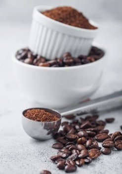 Fresh raw organic coffee beans in white bowl and powder on ligh table background and round steel scoop.