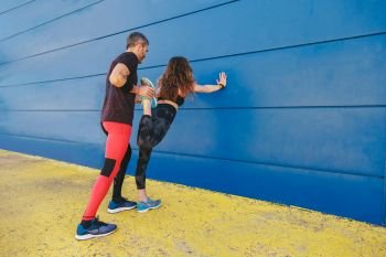 young couple stretching together in front of a blue wall before running