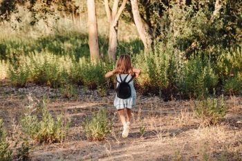 Young blonde girl running in the field wearing a dress with a magnifying glass in her hand an backpack