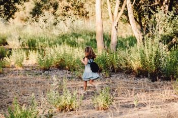 Young blonde girl running in the field wearing a dress with a magnifying glass in her hand an backpack