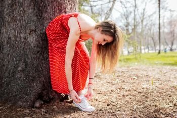 Young smiling blond woman leaning tying her sneakers whit dress
