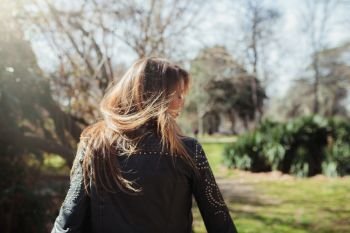 Young blonde woman from behind wearing a leather jacket in the park moving her hair