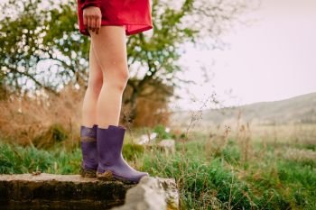Closeup outdoors of girl legs with red raincoat and water boots