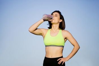 Girl drinking water wearing sporty clothes in the field