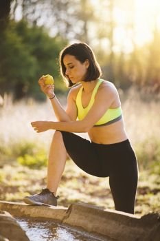 Young sporty woman eating an apple in the field at sunset after running