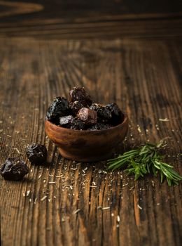 Marinated Olives with herbs and rosemary in a bowl on a wooden background
