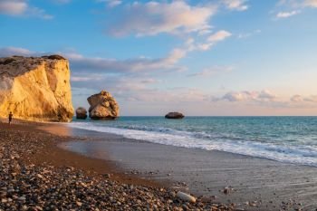 Beautiful afternoon view of the beach around Petra tou Romiou, in Paphos, Cyprus with a boy strolling in the distance. It is considered to be Aphrodite’s birthplace in Greek mythology.