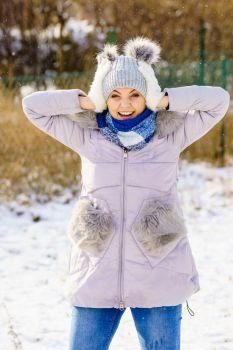 Pretty young woman wearing warm accessories during winter time. Female having grey beanie warm hat with pompons and pink jacket. Female wearing warm outfit during winter