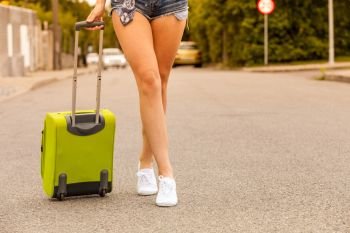 Travel, adventure, teenage journey concept. Woman wearing denim shorts and white sneakers walking with green suitcase. Attractive woman legs walking with green suitcase