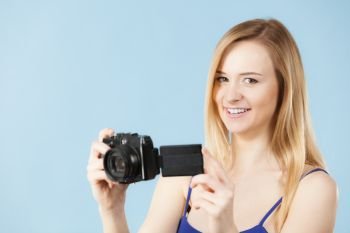 Photographer girl shooting images. Lovely blonde smiling woman with camera on blue background. Blonde woman with camera on blue