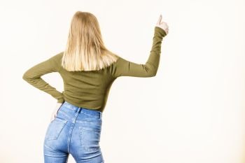 Back view of woman with blonde hair on white background showing something, pointing with finger at copy space.. Back view of woman pointing at copy space