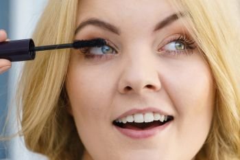 Woman doing her make up using black mascara brushing eyelashes. Female beauty visage concept.. Woman using mascara on her eyelashes