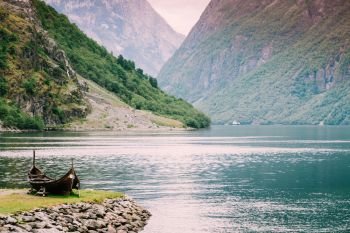 Old wooden viking boat on seashore in norwegian nature. Mountains and fjord Sognefjord. Tourism and traveling concept. Old wooden viking boat in norwegian nature