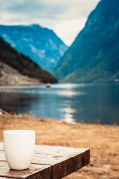 Mug on wooden table. Beautiful fjord norwegian scandinavian landscape in background, lake and mountains.. Mug on wooden table, fjord norwegian landscape