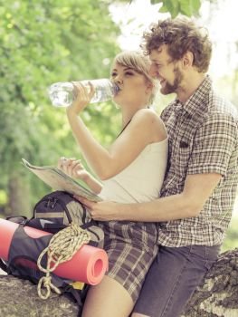 Adventure, tourism active lifestyle - young couple backpackers hikers resting in forest drinking water from plastic bottle