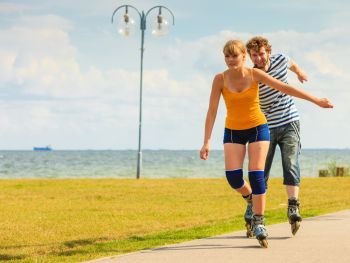 Active lifestyle people and freedom concept. Young fit couple on roller skates riding outdoors on sea coast, woman and man rollerblading enjoying time together