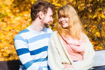 Concepts of autumn love togetherness and relationship. Young romantic couple sitting on bench hugging in autumnal park on sunny day . Lovers couple in autumn park on bench