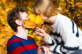 Love relationship dating and people concept - close up couple hiding behind maple leaf kissing in autumn park. couple with maple leaf kissing in autumn park