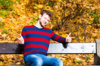Season, happiness and people concept. Young bearded man sitting relaxed on bench in autumnal park on sunny day . man sitting on the bench in park