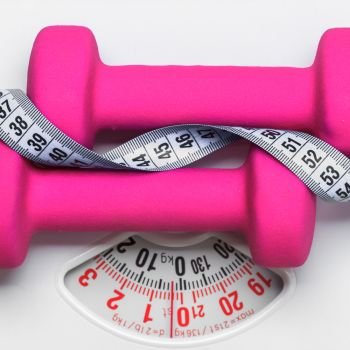 healthy lifestyle fitness weight control concept. Closeup pink dumbbells with measuring tape on white scales