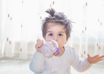 Portrait of adorable cute little baby girl toddler holding and drinking water from a bottle. Portrait of adorable cute little baby girl