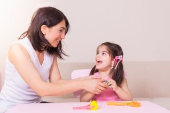Happy beautiful mother and cute girl playing together with playdough while sitting on table. . Mother and Cute girl playing together with playdough